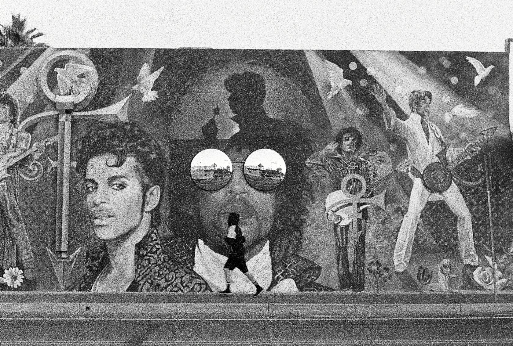 A black and white photo of a mural Grand Avenue Phoenix depicting career of Prince. Unidentifiable jogger in foreground.